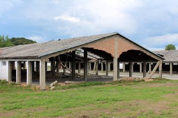 Densely built wide large hangar buildings with missing destroyed red brick support walls and unusual bent roofs surrounded with paved area mixed with grass and trees at abandoned military complex