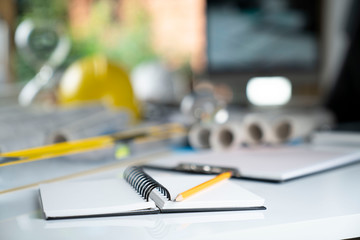 Architecture and construction concept. Empty notebook, rolls with building projects, spirit level  and architect yellow helmet on tabletop.