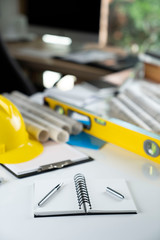 Fototapeta premium Architecture and construction concept. Empty notebook, rolls with building projects, spirit level and architect yellow helmet on tabletop.
