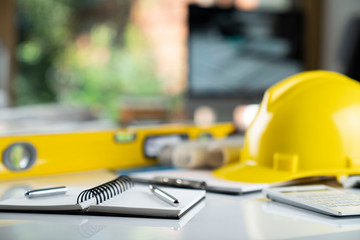 Fototapeta premium Architecture and construction concept. Empty notebook, rolls with building projects, spirit level and architect yellow helmet on tabletop.