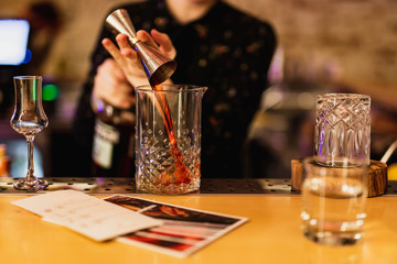 Bartender prepairing a cocktail at the bar. Pouring alcohol into the mixing glass using jigger. Selective focus, lifestyle.