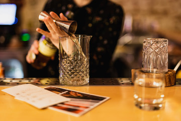 Bartender prepairing a cocktail at the bar. Pouring alcohol into the mixing glass using jigger. Selective focus, lifestyle.