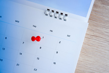 Thumbtack a date on calendar on the table with wooden background, concept for important date, meeting reminder, planning for business, travel planning concept