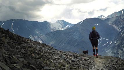 Fototapeta premium A man and a dog running in the mountains on a stone path.