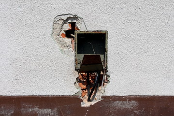 Rectangle empty plastic electrical outlet box with broken cover and cut wires mounted on cracked family house wall on warm sunny summer day