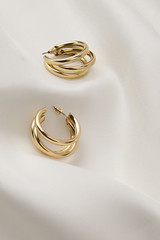 Subject shot of a pair of golden stud earrings isolated on the white textile surface. Each earring...