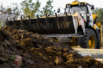 Excavation works at the construction site. Bulldozer or a backhoe loader dumping ground into the...