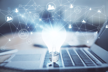 Computer on desktop in office with bulb icon hologram. Multi exposure. Concept of idea.
