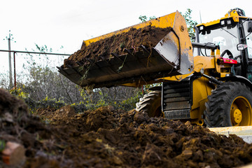 Excavation works at the construction site. Bulldozer or a backhoe loader dumping ground into the...