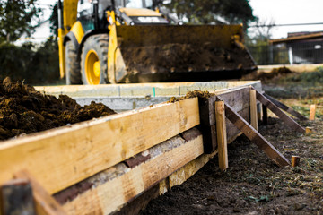 Fototapeta premium Excavation works at the construction site. Bulldozer or a backhoe loader dumping ground into the falsework. Low-rise construction. Foundation of small cottage