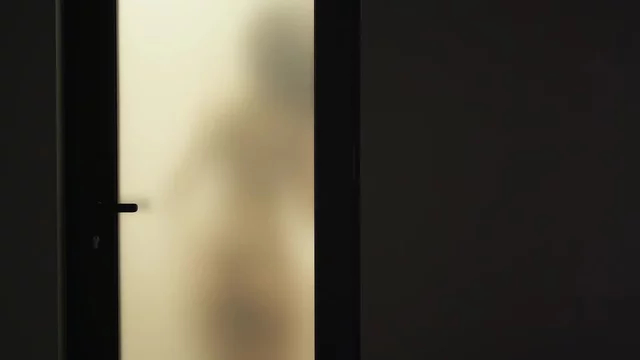 Woman behind blurry glass door. Girl taking off bra and panties