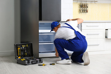Male technician repairing broken refrigerator in kitchen