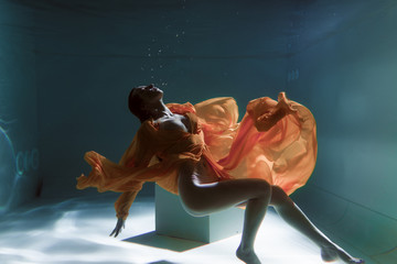 Beautiful girl swims underwater in a yellow dress. 2020 New Year trend Aqua Mente and fatom blue...