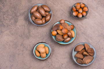 Different nuts, pecan nuts, hazelnuts, almonds and brazil nuts on a brown textured background, empty copy space