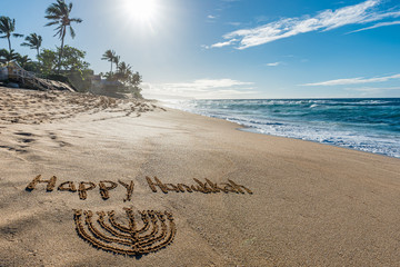 Happy Hanukkah written in the sand with a Hanukkiah with a tropical beach and ocean in the...