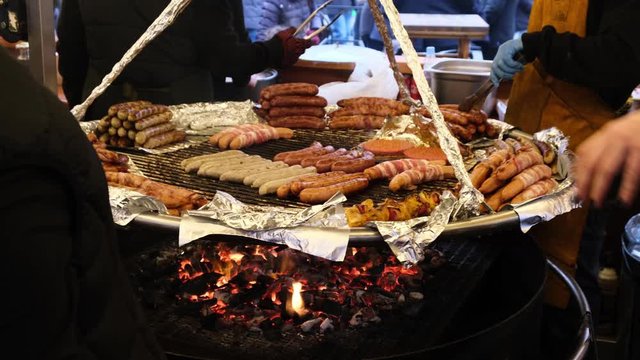 Vendors fry fresh grilled sausages and barbecue on a big round pan on open fire in outdoor cafe. Treat for a hungry tourists at the fair