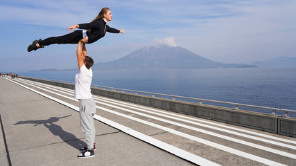  A young couple of acrobats on a background of a smoking volcano doing gymnastic support. beautiful...