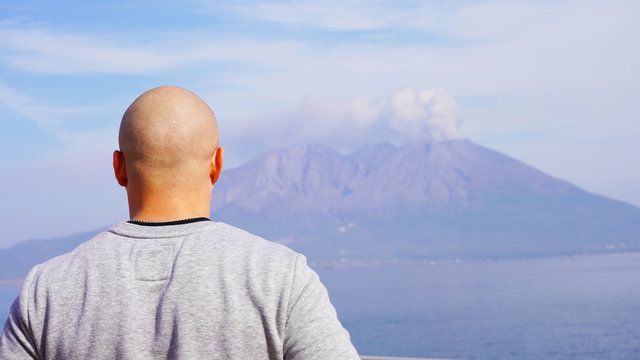bald guy in casual clothes on a background of a smoking volcano on a sunny day in Japan. volcano eruption 
