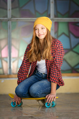 Lifestyle vertical outdoor portrait of young smiling teenage girl  with a yellow skateboard