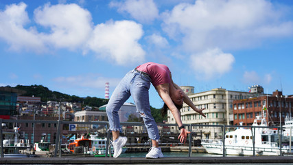 young beautiful flexible girl in the city on the embankment stands in a bridge pose. gymnast in...