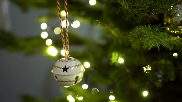 Decoration on the Christmas tree. White christmas bell with a zig zag pattern swinging on a branch of a illuminated Christmas tree.