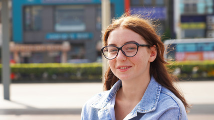 Young girl model with glasses laughing on a sunny day over a cup of coffee. beautiful girl in a denim jacket smiles and drinks coffee on the street