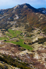 Fototapeta na wymiar small house with a red roof among the emerald green alpine meadows and stones far below, a symbol of solitude of peace and unity with nature.