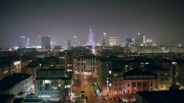 Drone flies over the nightly architecture of downtown Warsaw. Aerial view of a cityscape on a foggy night in the center of Warsaw-Poland. 