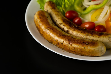 Two long grilled bratwurst sausage with mix vegetables salad in the white plate isolated on black background