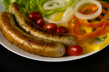 Two long grilled bratwurst sausage with mix vegetables salad in the white plate isolated on black background