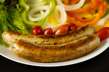 Two long grilled bratwurst sausage with mix vegetables salad in the white plate isolated on black background