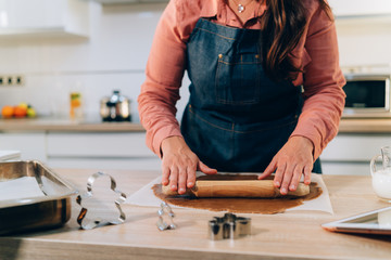 Young brunette woman knead a dough for making cookies at home for the Christmas Holidays. Handmade gingerbread cookies