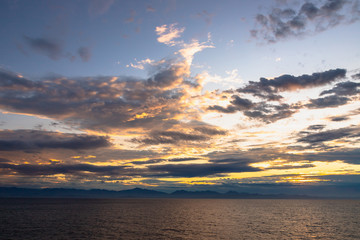 A dramatic set of clouds, at sunset, drifting over the tropical waters of the Caribbean Sea are lit by the last moments of daylight.