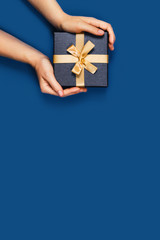 Gift box with surprise in a female hands on classic blue background. Flat lay, top view, place for text.