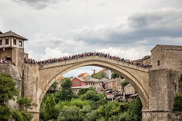 Fotobehang Stari Most Een man springt van de oude brug &quot Stari Most&quot  terwijl het publiek op de brug hem toejuicht, Mostar, Bosnië en Herzegovina