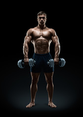 Fototapeta na wymiar Handsome power athletic man bodybuilder doing exercises with dumbbell, confidently looking forward. Fitness muscular body on dark background.