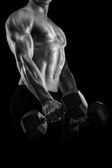 Obraz na płótnie Canvas Handsome power athletic man in training pumping up muscles with dumbbell. Strong bodybuilder with six pack, perfect abs, shoulders, biceps, triceps and chest. Black and white photo.