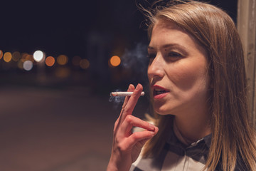 Close up portrait of young caucasian woman smoker on the street at night with cigarette smoking in the city outdoor smoke enjoining