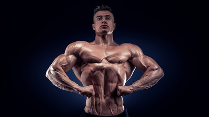Fototapeta na wymiar Handsome muscular bodybuilder posing on Front Lat Spread display lat width from the front, chest thickness, shoulder width, front arm and forearm size, quadriceps mass and separation