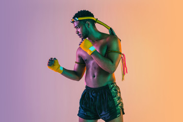 Muay thai. Young man exercising thai boxing on gradient background in neon light. Fighter...