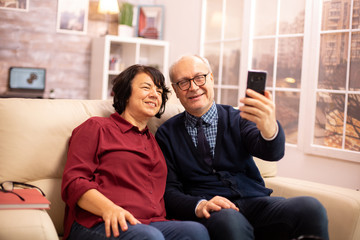 Fototapeta na wymiar Beautiful elderly couple taking a selfie while sitting on the couch