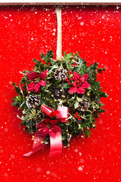 Amazing Christmas wreath with big red bow, Red Christmas Poinsettia flowers and Holly Berries on red door, Xmas celebration concept