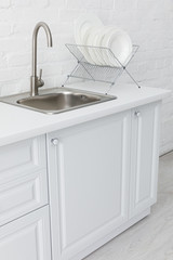 minimalistic modern white kitchen interior with sink and plates on stand near brick wall