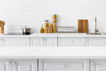 selective focus of empty tabletop and minimalistic modern white kitchen interior with kitchenware...