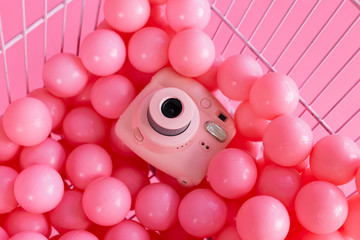A pink instant camera lies in a trolley among pink balls
