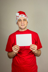  young guy in christmas hat and red t-shirt with white card in his hands for inscription