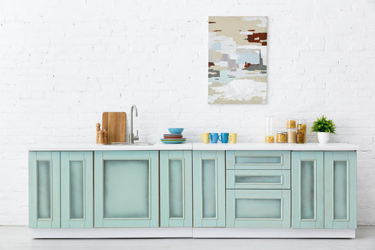 white and turquoise kitchen interior with kitchenware and abstract painting on brick wall