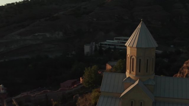 Aerial view of the dome cross of Narikala fortress in sunshine sunset drone.