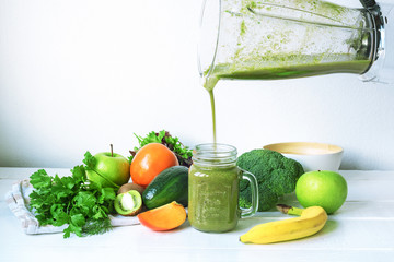 Green smoothie is poured from a blender bowl into a glass jar. Healthy raw vegan food concept.