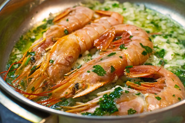 Big langoustines with oil and herbs on the frying pan. Roasted king prawns or tiger shrimps with green herbs.